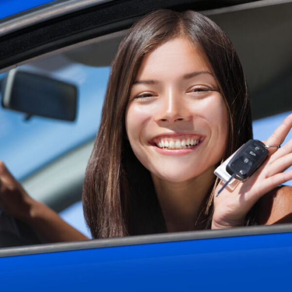 Happy Asian girl teen driver showing new car keys. Young woman smiling driving new car holding key. Interracial ethnic woman driver holding car keys driving rental car.